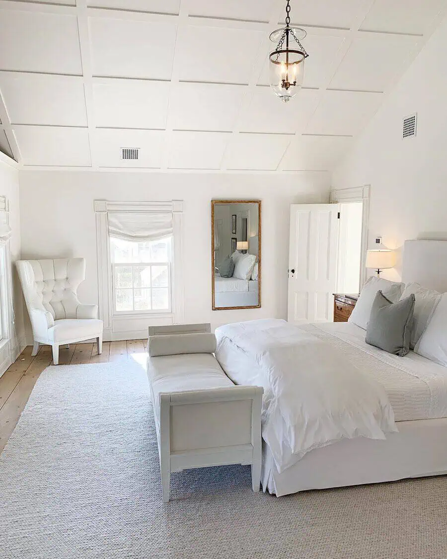 Bright, airy bedroom with white furniture, a large mirror, and a tufted armchair, creating a serene atmosphere.