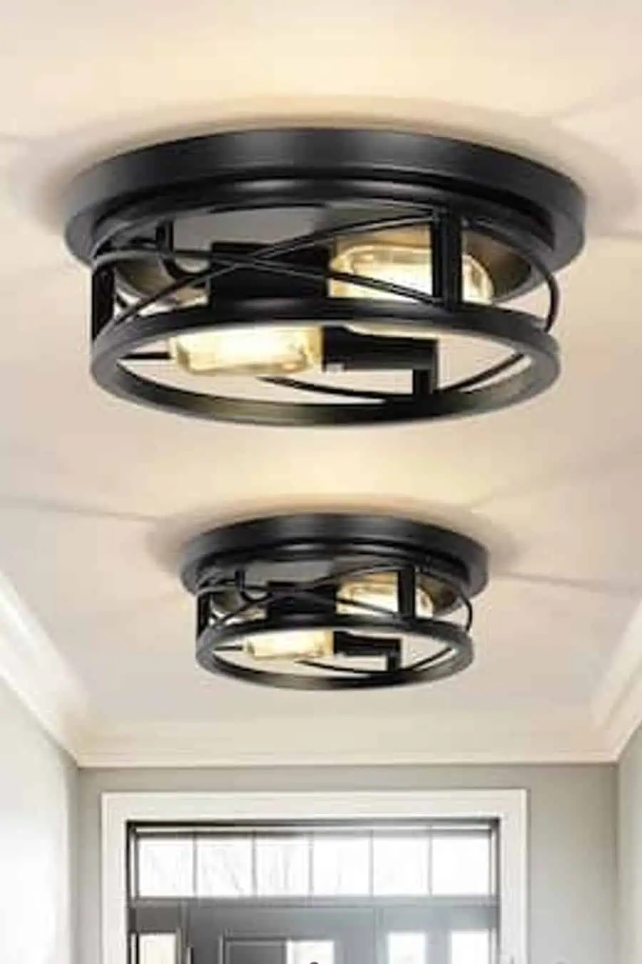 A modern entryway featuring sleek, black metal flush-mount chandeliers that provide warm, ambient lighting.