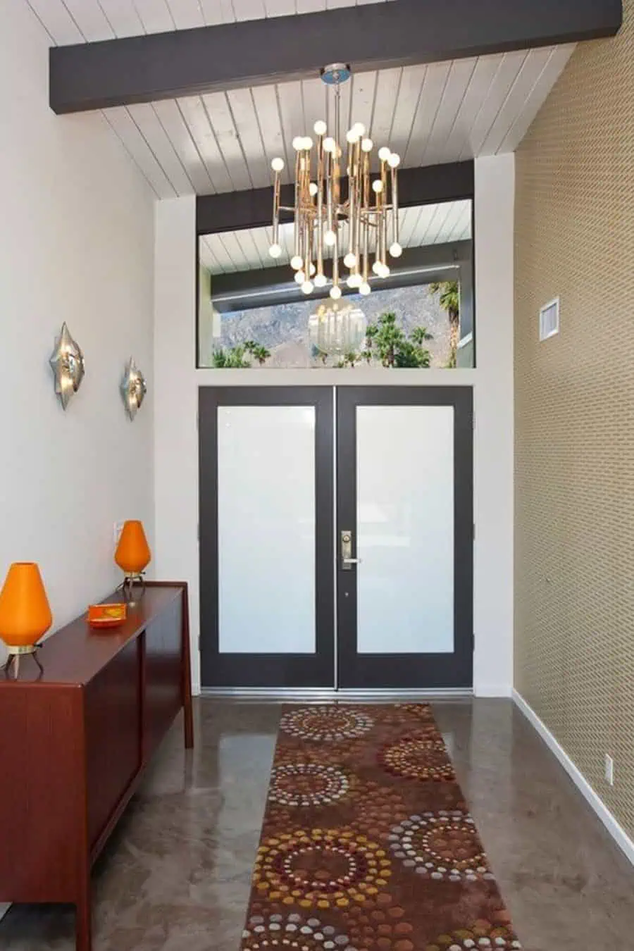 A mid-century modern entryway with a chandelier featuring multiple glowing bulbs, providing warm lighting.