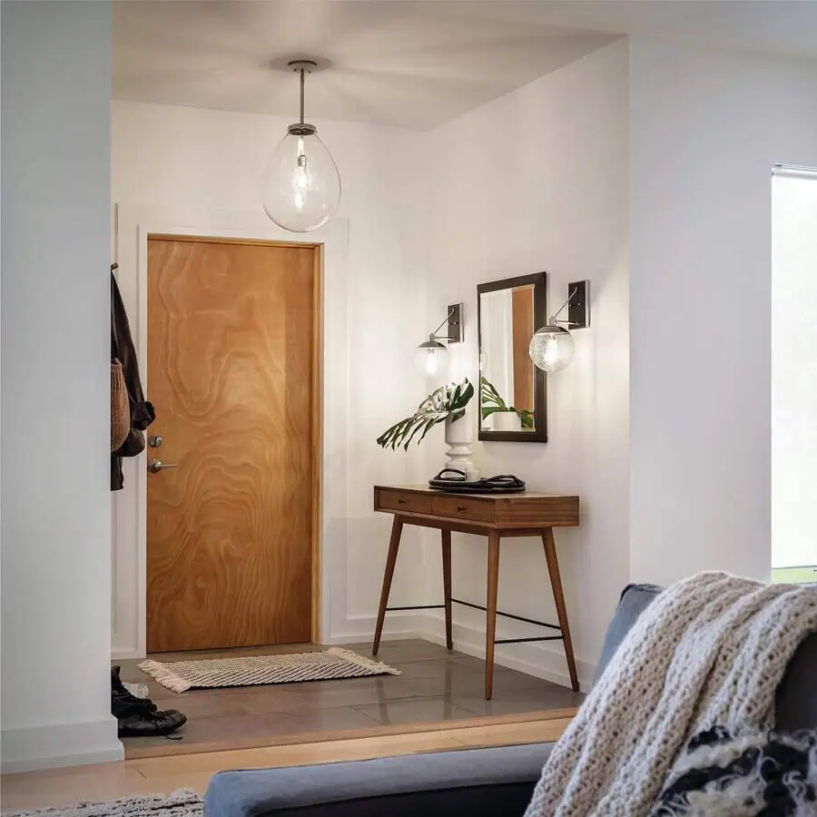 Entryway with a wooden door, console table and mirror, hanging light fixtures, and a small rug