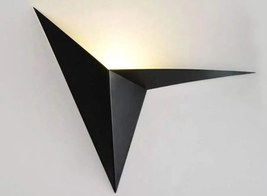 A modern black geometric wall light fixture with asymmetrical triangular shapes emitting light from its center