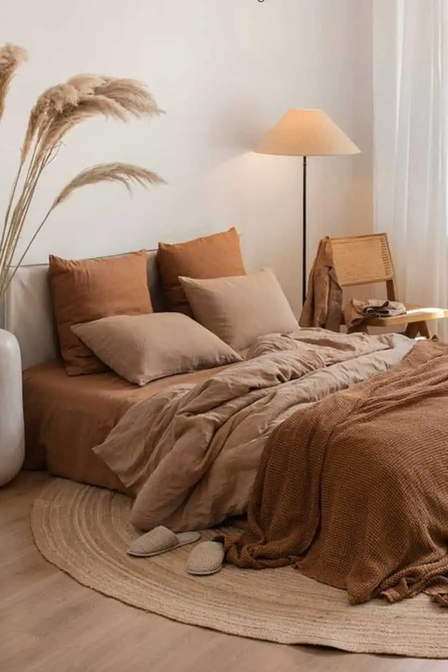 Cozy bedroom with earthy-toned bedding, a floor lamp, a circular rug, and pampas grass decor.