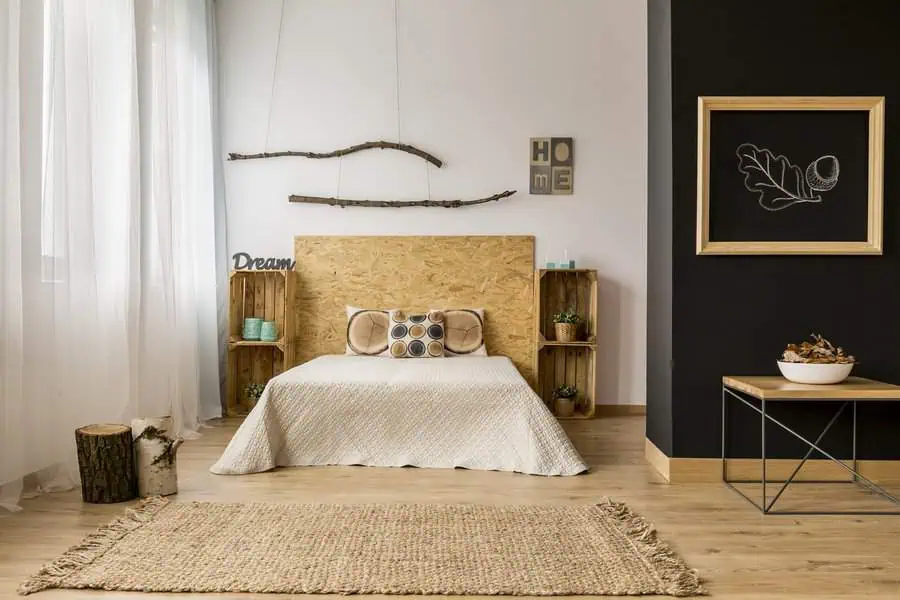 Minimalist bedroom with a wooden bed, light quilt, decorative pillows, wall art, and rustic decor on a black accent wall