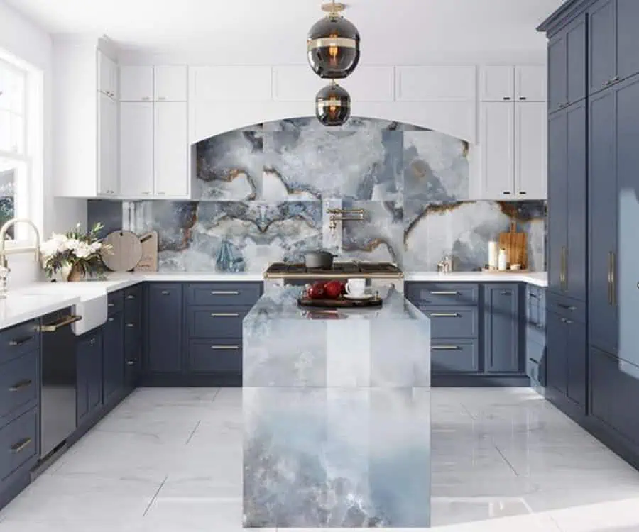 A kitchen with blue and white cabinetry, a striking marble-patterned island and backsplash, and pendant lights.