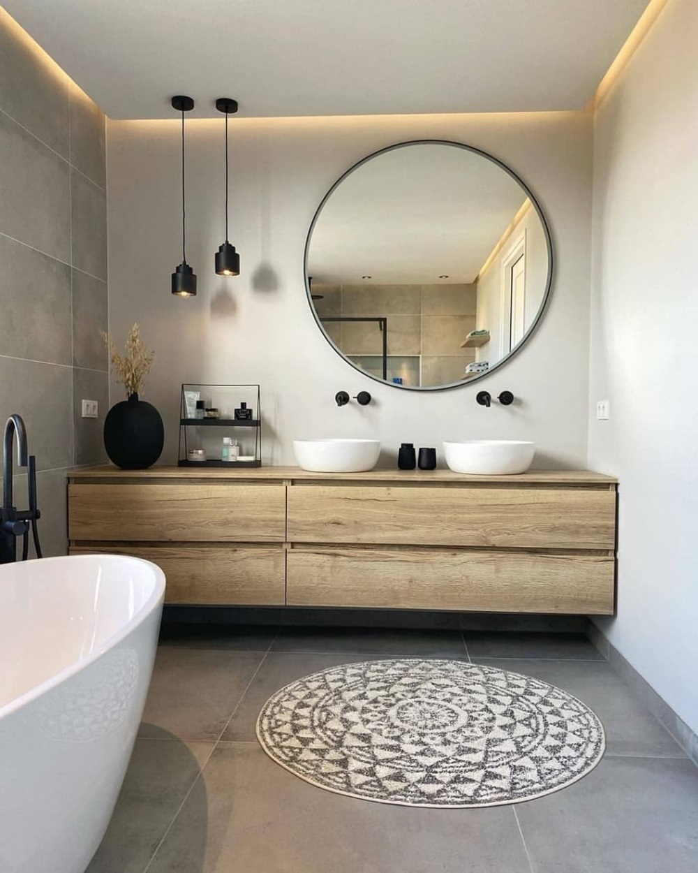 Modern bathroom featuring a round mirror, double sinks, pendant lights, and a decorative rug