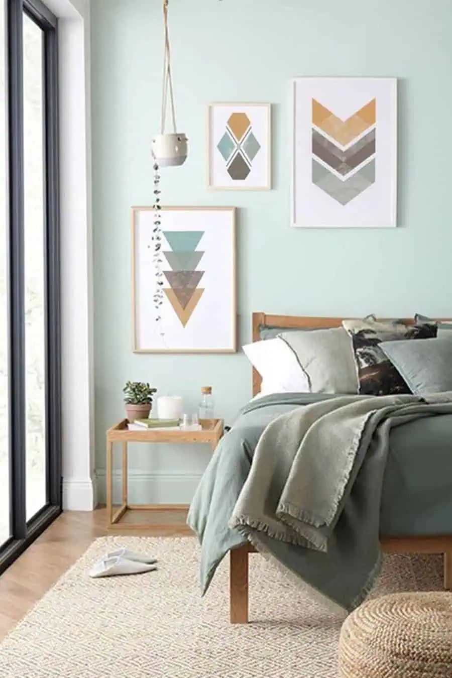 A modern bedroom with framed prints, a bedside table, and light green bedding