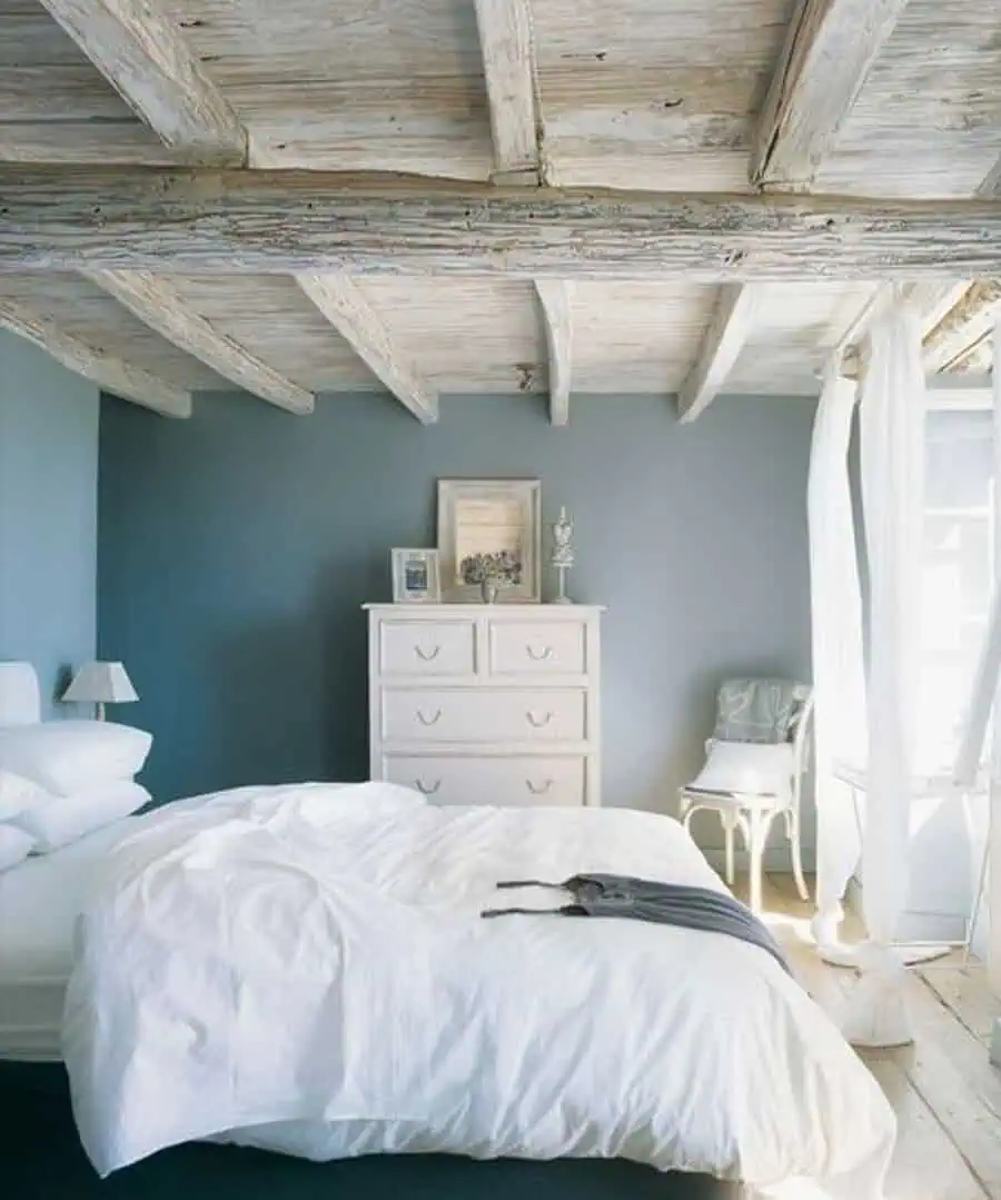 A cozy bedroom with a wooden ceiling, light blue walls, and white furniture and bedding