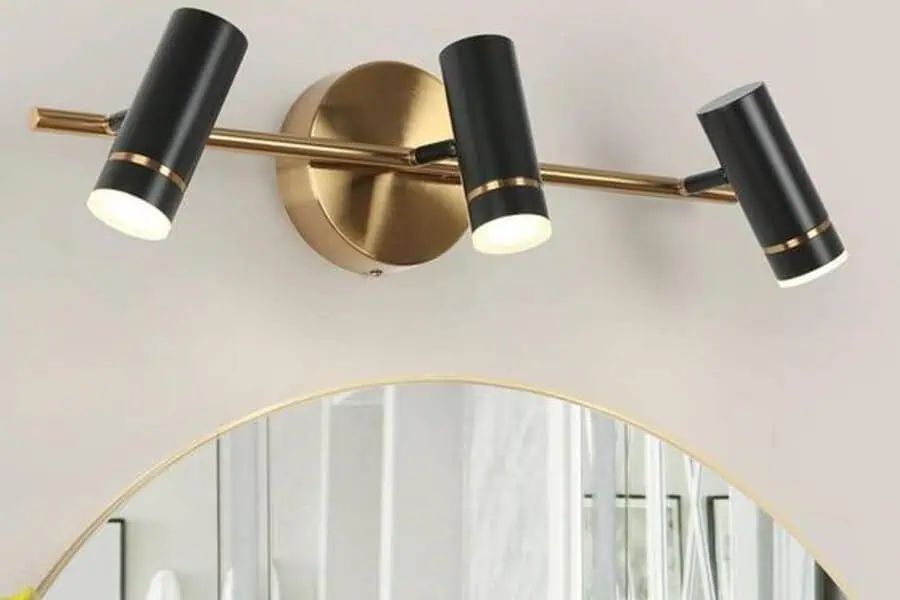 Black and gold three-light wall fixture above a round mirror with a gold rim