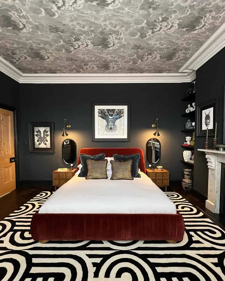 A stylish bedroom with dark walls, a patterned ceiling, a red velvet bed, and black-and-white geometric rug