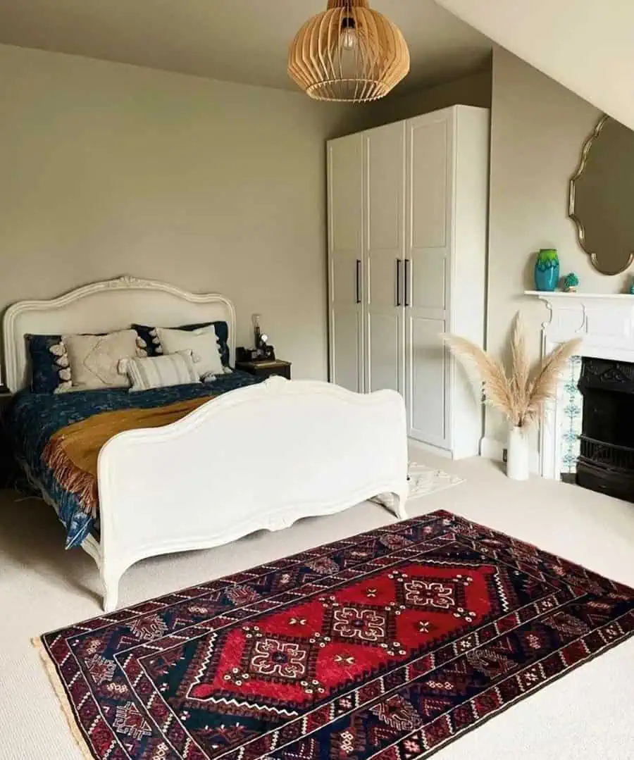 Cozy bedroom with white bed, colorful rug, wooden hanging lamp, and white wardrobe next to decorative vase and fireplace