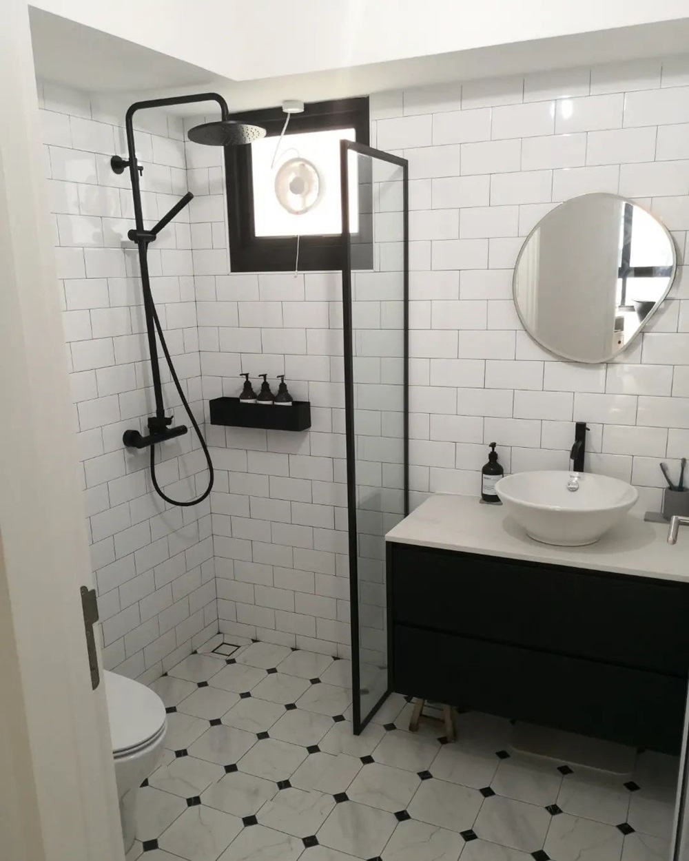 Modern bathroom featuring a black shower, white tiles, round mirror, and vanity sink