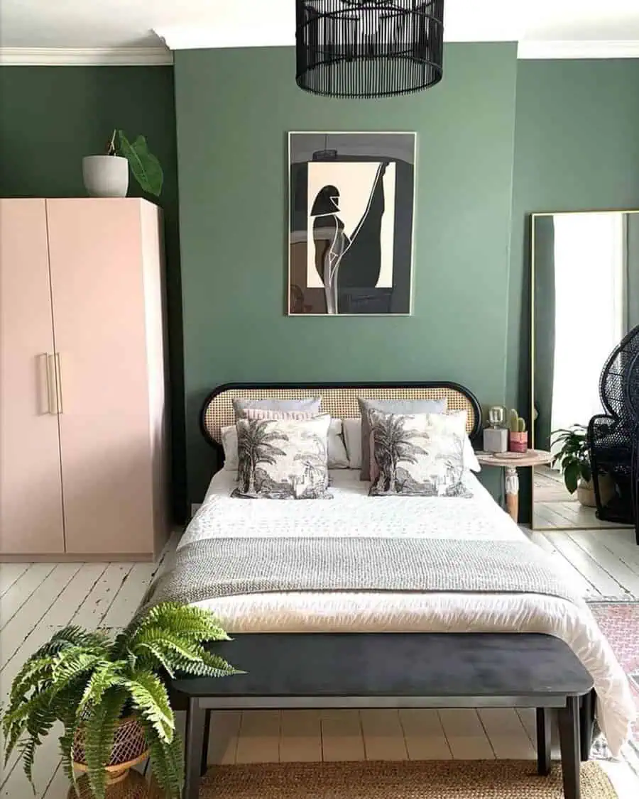 Bedroom with green walls, a bed with printed pillows, plants, a pink wardrobe, a large mirror, and abstract artwork