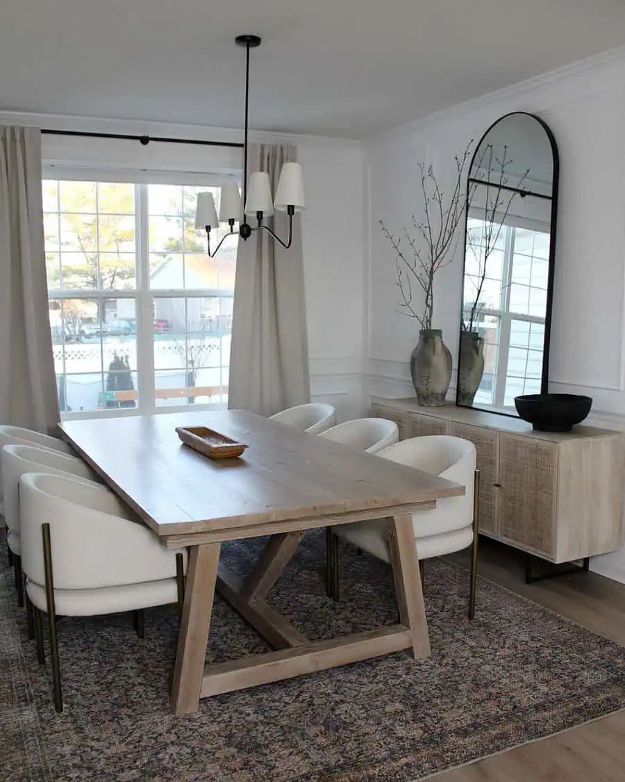 A modern dining room with a wooden table, white chairs, a chandelier, a large mirror, and vases on a sideboard