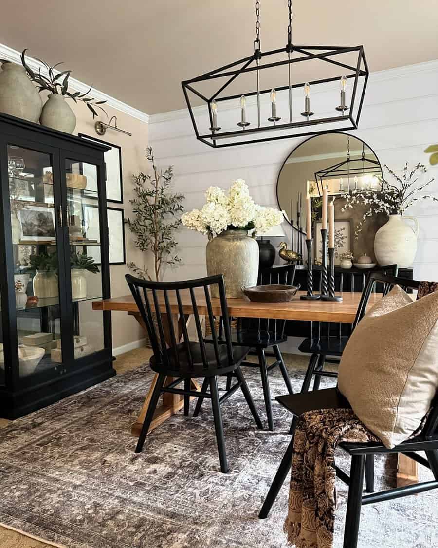 Modern dining room with black chairs, wooden table, large floral arrangements, black chandelier, and decorative cabinet