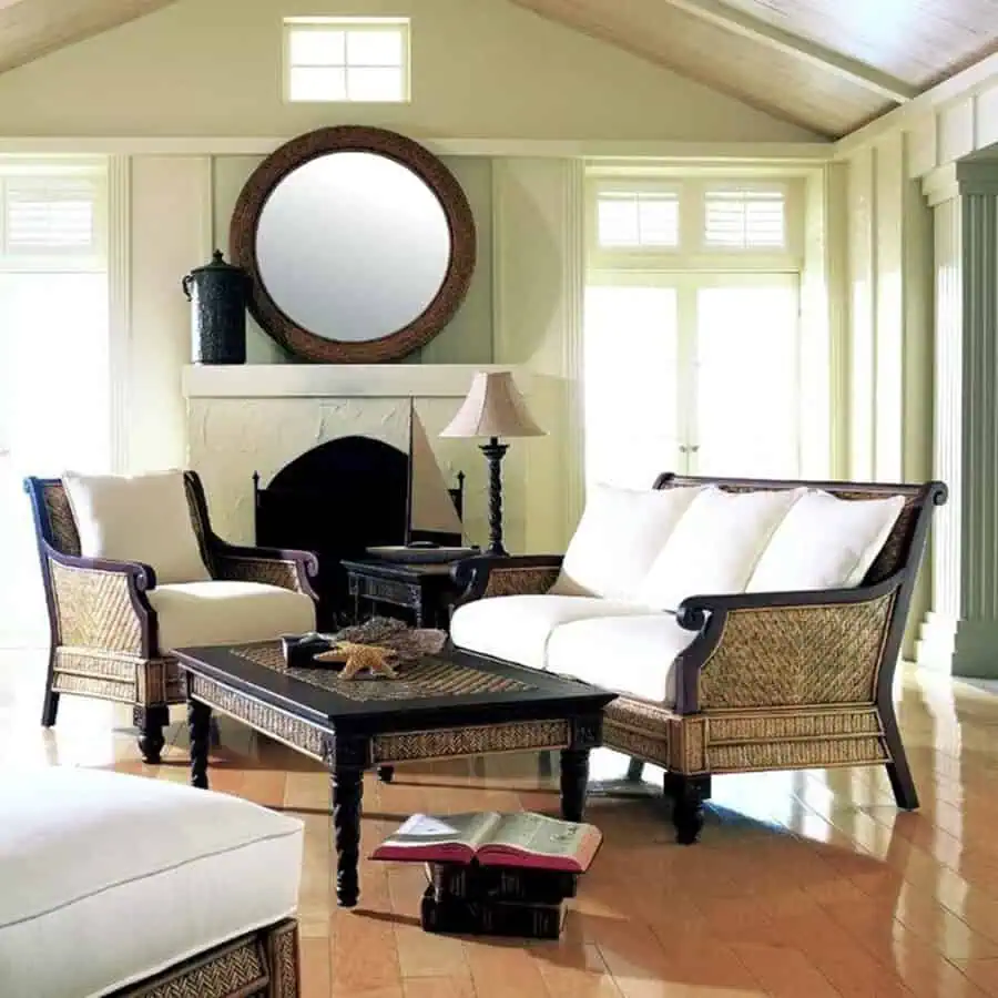 Elegant living room with wicker furniture, white cushions, and a round mirror above the fireplace