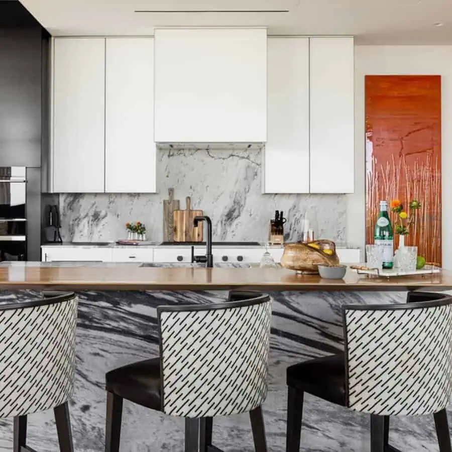 Modern kitchen featuring white cabinets, marble backsplash, and island with black and white patterned chairs