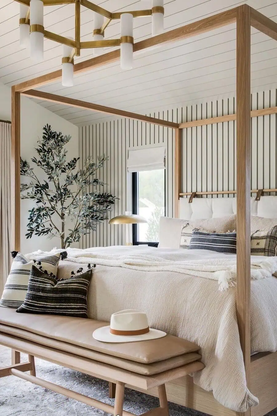 Bedroom featuring a four-poster bed, striped cushions, a bench with a hat, a potted plant, and a modern chandelier