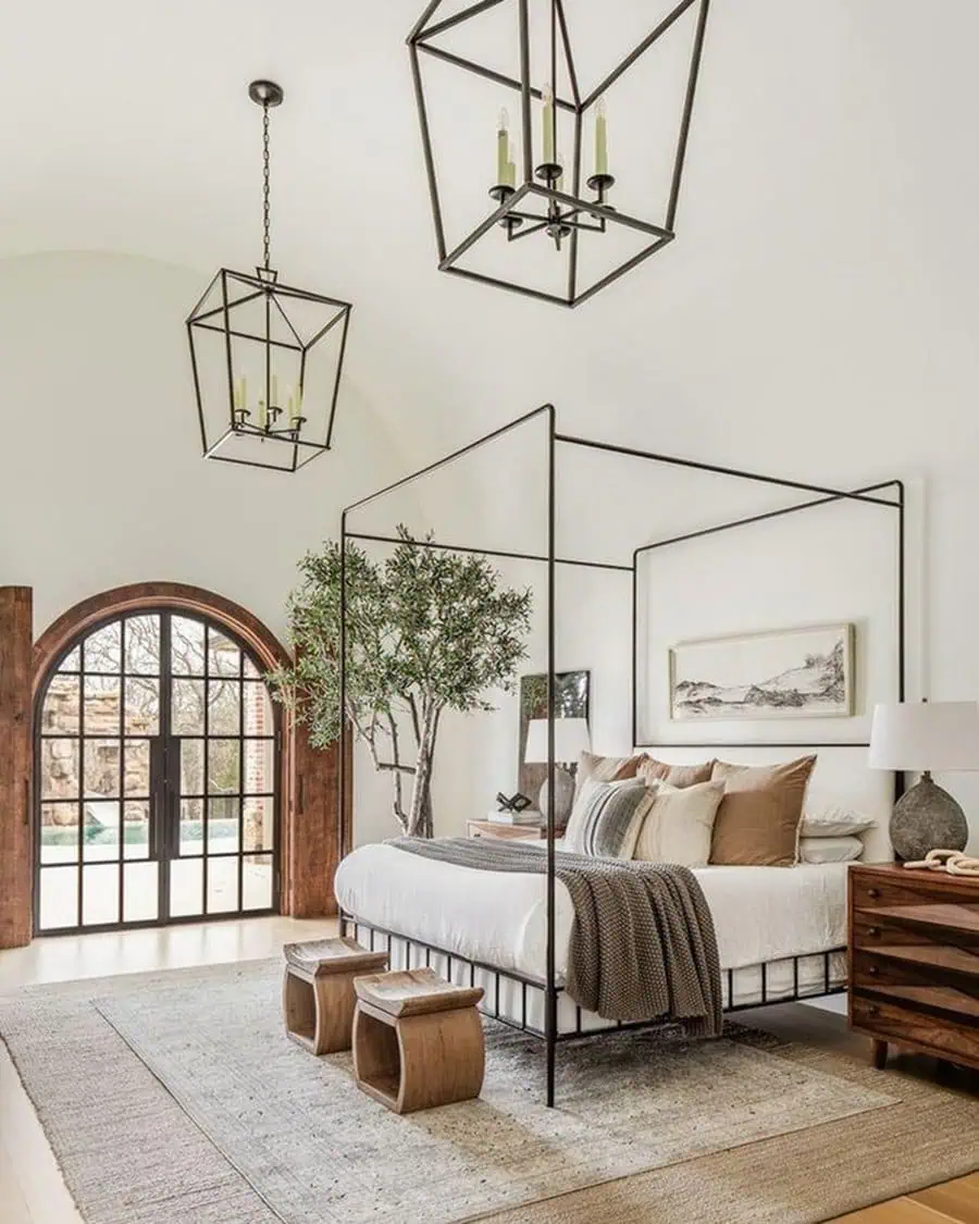 Modern bedroom featuring a canopy bed, wooden nightstands, large arched window, geometric chandeliers, and a potted tree