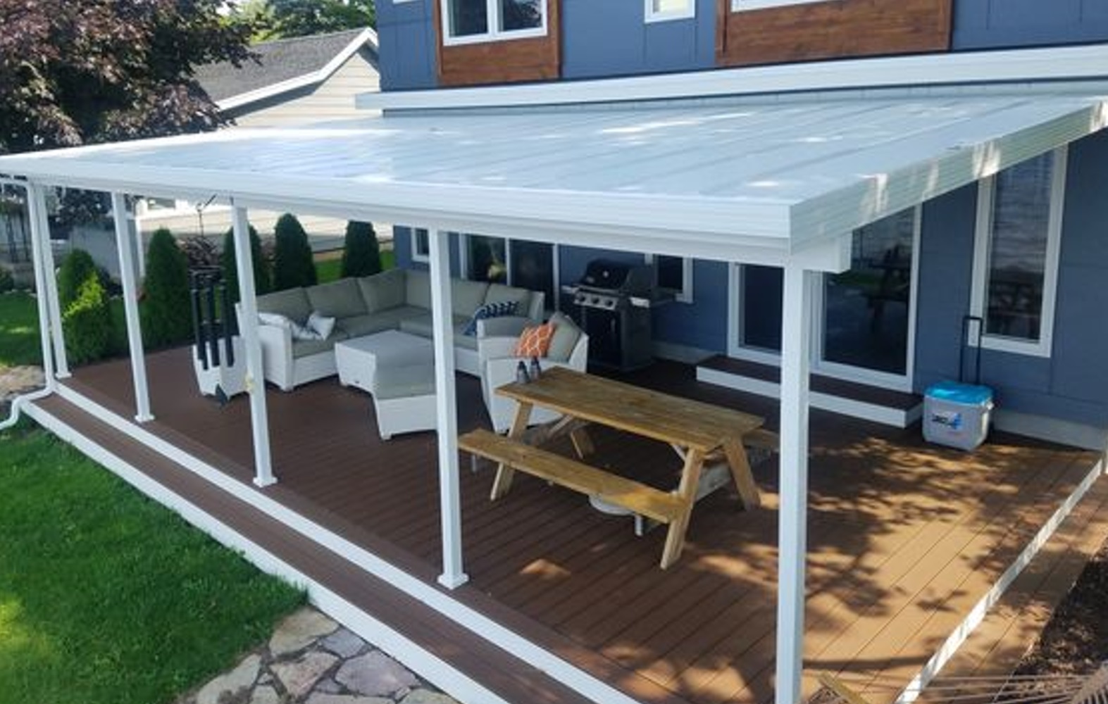 Covered patio with seating, a wooden picnic table, and a barbecue grill