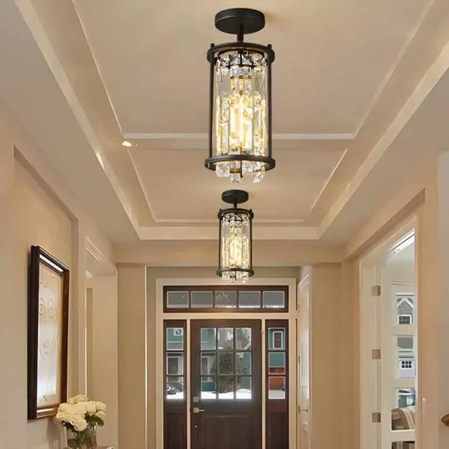 Elegant hallway featuring two modern chandeliers, a dark wooden front door with glass panels, and neutral-colored walls