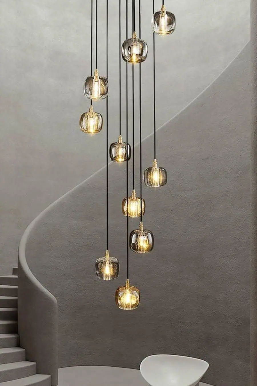 Modern pendant lights with clear glass bulbs hanging from a high ceiling next to a spiral staircase with smooth walls