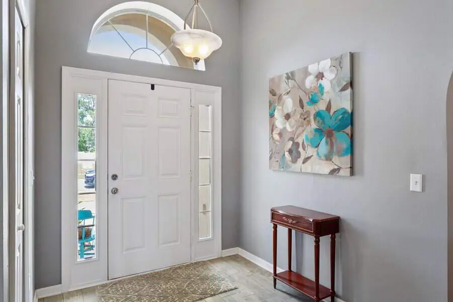 Entryway with white front door, glass side panels, floral artwork on wall, small wooden table, and gray walls