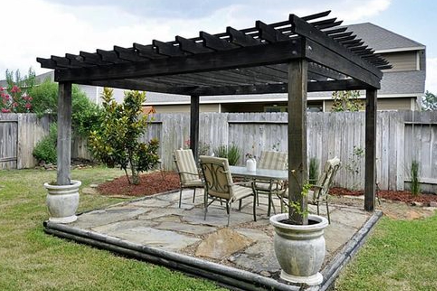 Wooden pergola with patio furniture in a fenced backyard