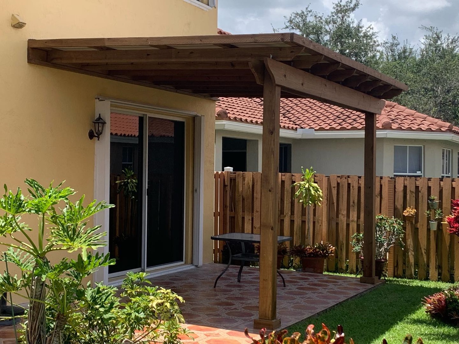 A covered patio with wooden pergola and plants in a backyard on a sunny day