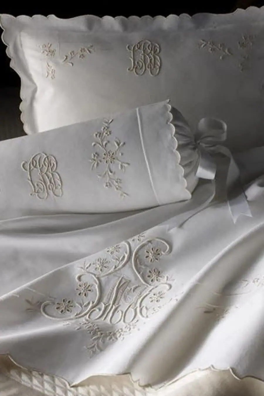 White embroidered bedding with intricate floral designs and monogrammed initials.