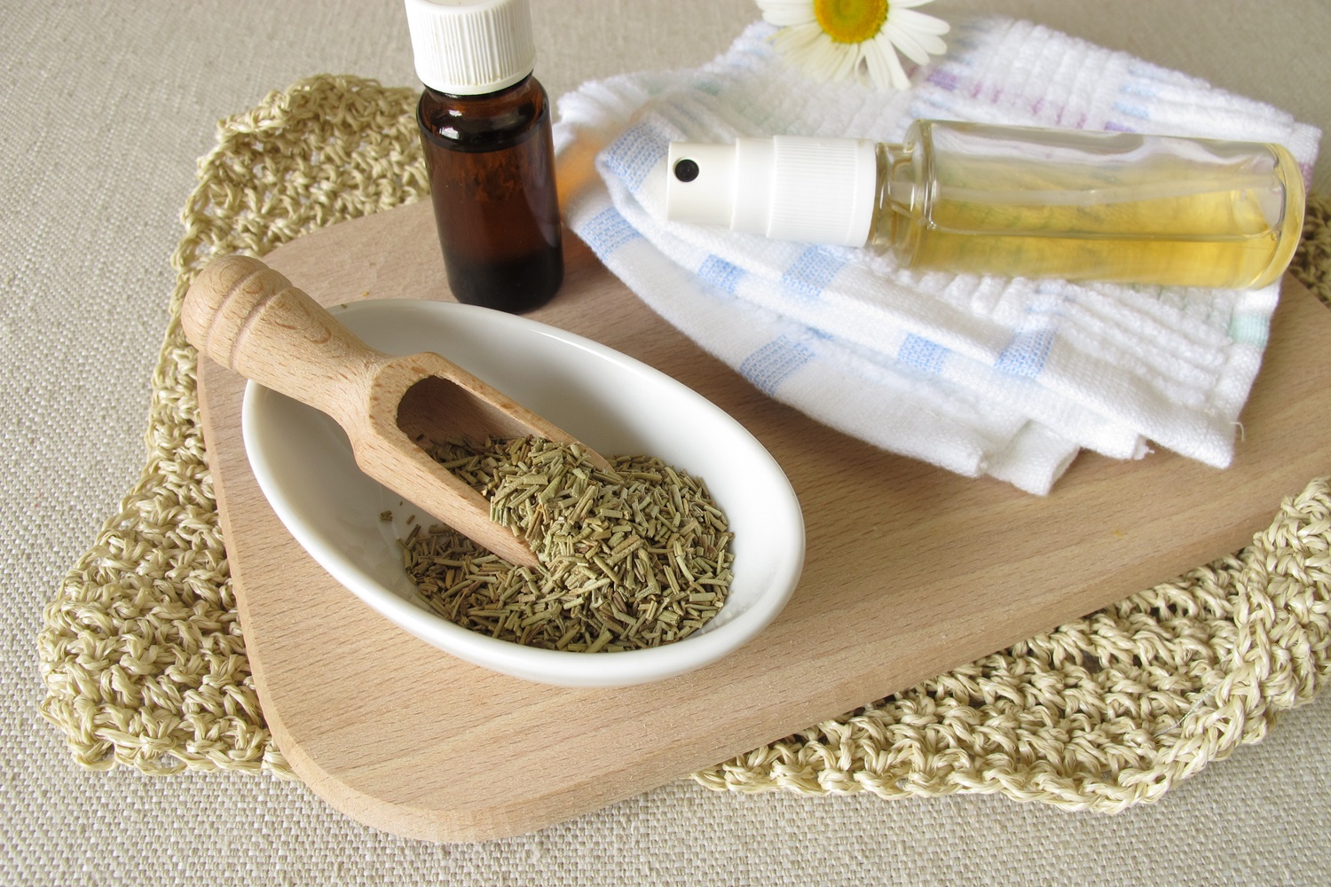 Herbs in a dish with essential oil bottles and towels on a wooden tray