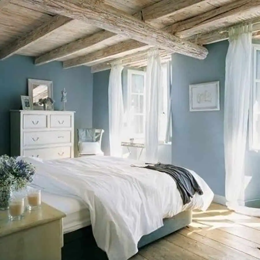 Rustic bedroom with wooden exposed beams, white dresser, and sunlight streaming through sheer curtains