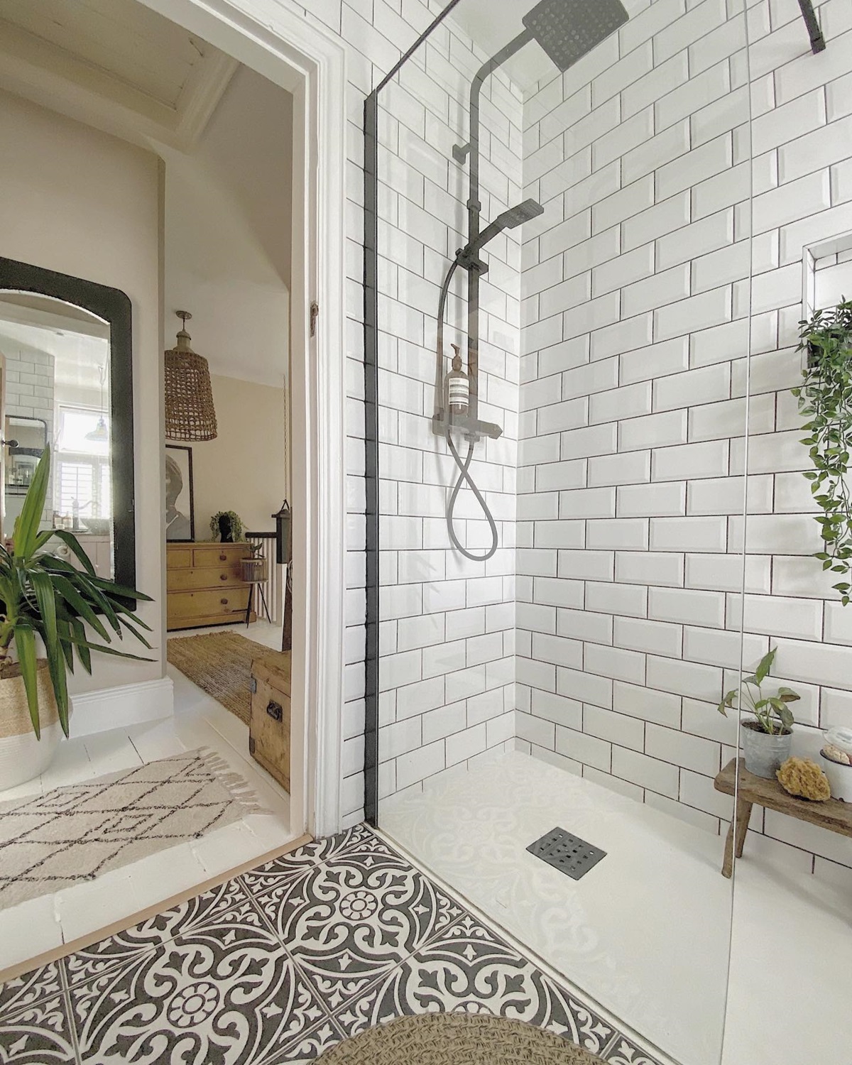 A modern bathroom with white subway tiles and a glass shower door next to a cozy room