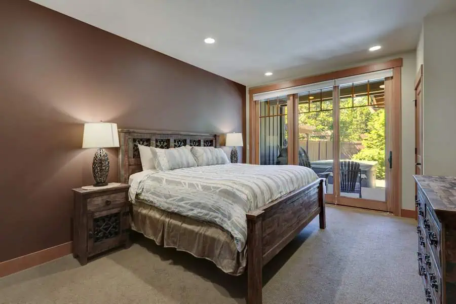 Cozy bedroom with wooden furniture, large bed, lamps, and glass doors leading to an outdoor area.