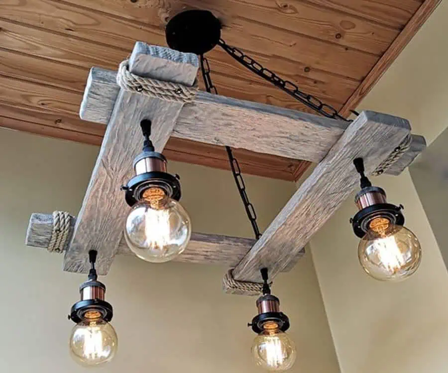 Wooden chandelier with four hanging exposed lightbulbs, mounted on a wooden ceiling with ropes and chains