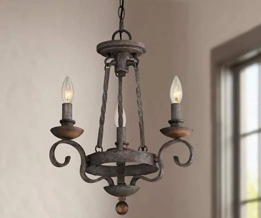 Rustic, wrought iron chandelier with three candle-shaped light bulbs hanging in a room near a window