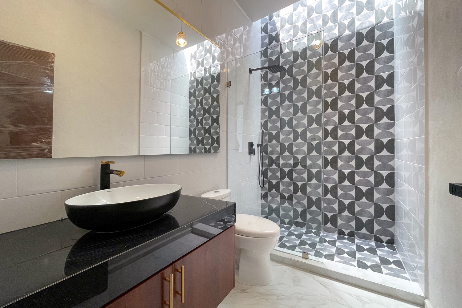 Modern bathroom with vessel sink, black countertop, and patterned shower tiles