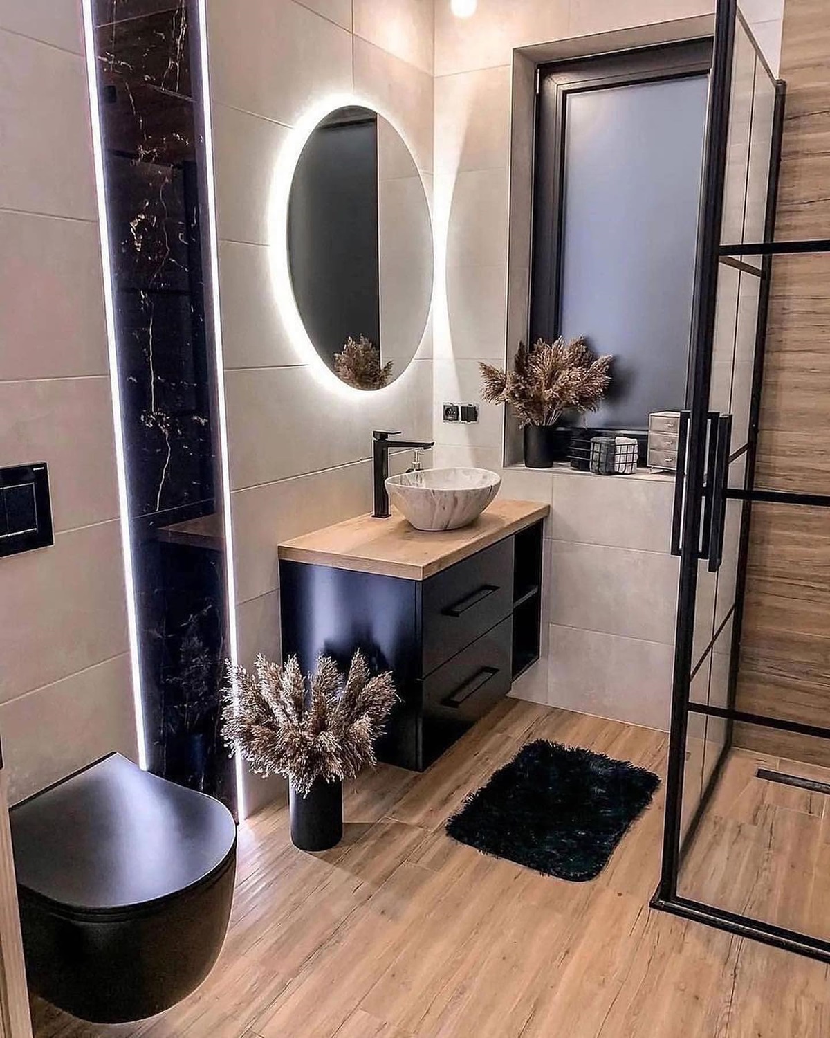 Modern bathroom featuring a round backlit mirror, black fixtures, and wooden accents