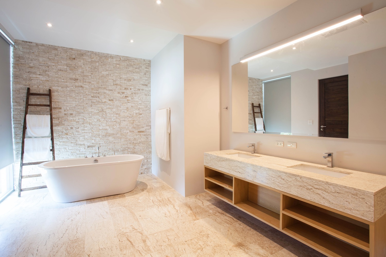 Modern bathroom featuring a bathtub, dual sinks, and a towel ladder against a brick wall