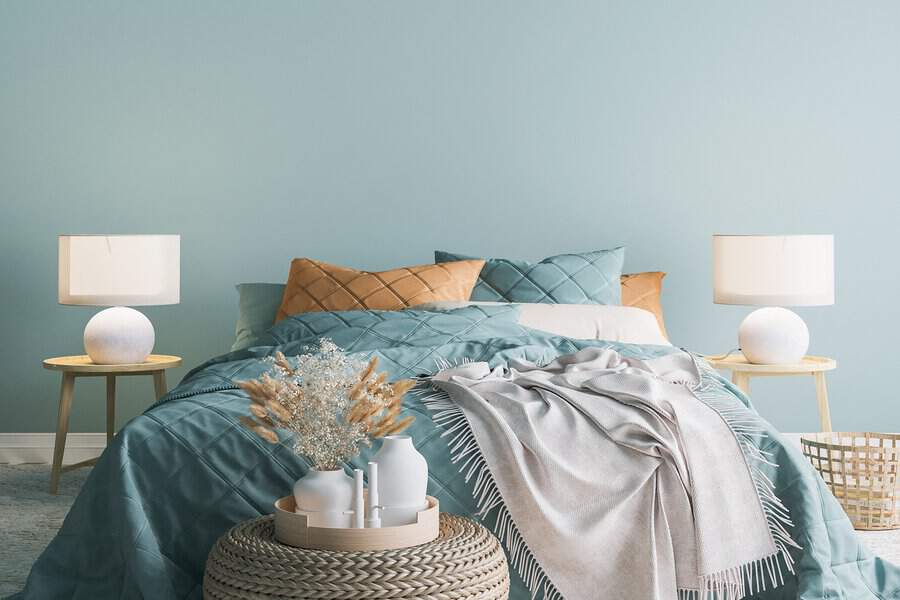 A bedroom featuring teal bedding, beige pillows, bedside tables with lamps, and various decorative elements