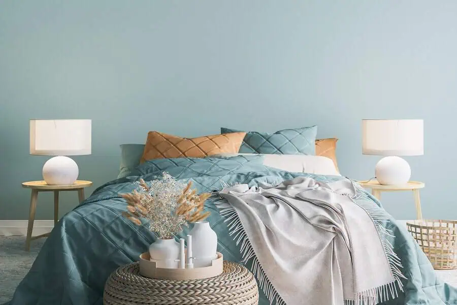 A bedroom featuring teal bedding, beige pillows, bedside tables with lamps, and various decorative elements