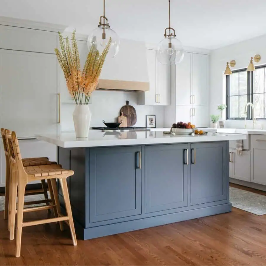 A modern kitchen with a navy island, wooden stools, and glass pendant lights above the counter.