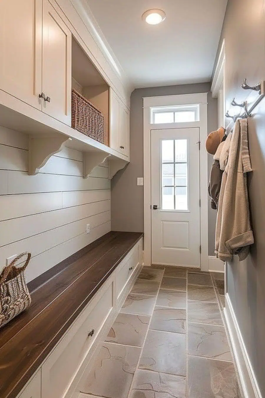 Bright entryway with a wooden bench, hooks, and storage cabinets; coats and hats hanging by the door