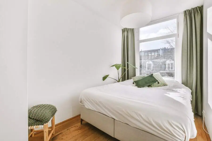 Bright and minimalistic bedroom with white walls, green curtains, and a small bed with green accent pillows.