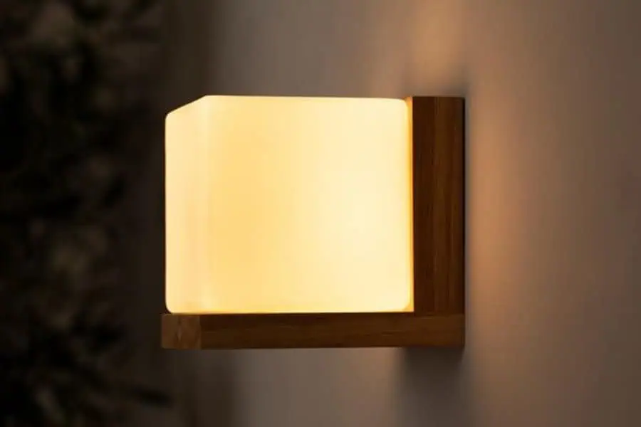 A wall-mounted wooden lamp with a glowing rectangular light fixture emits a soft, warm light