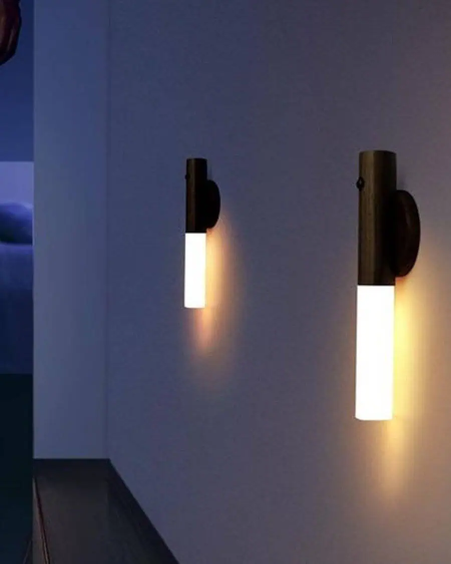 Two modern wall sconces with cylindrical lights mounted on a dimly lit hallway wall