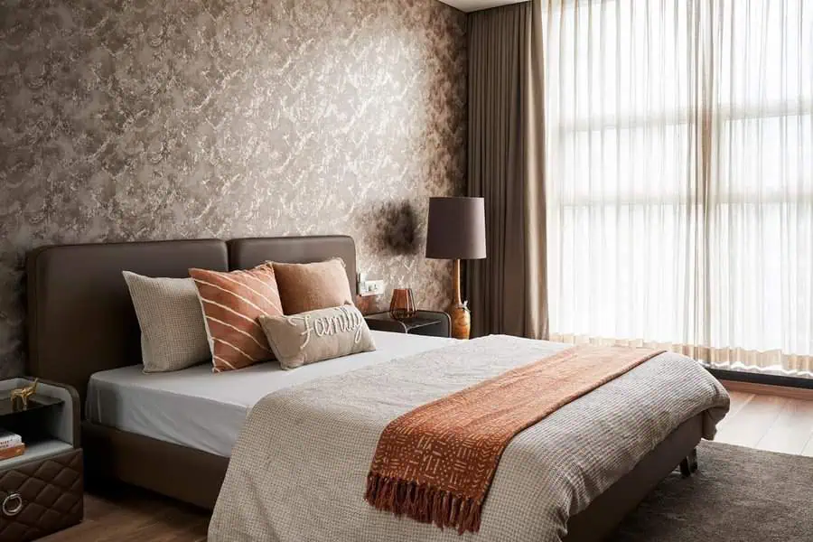 Cozy bedroom with a double bed, patterned wallpaper, and light pouring through tall windows.