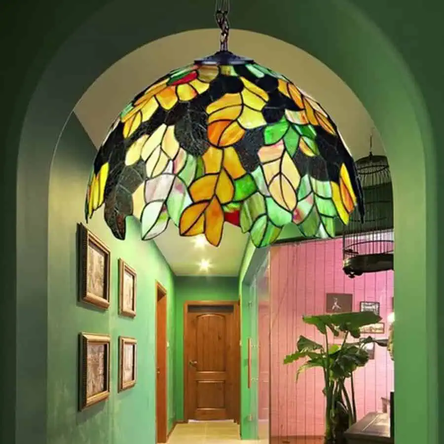 A vibrant hallway with green walls, featuring a colorful stained-glass pendant light in a leafy design, creating a striking focal point.