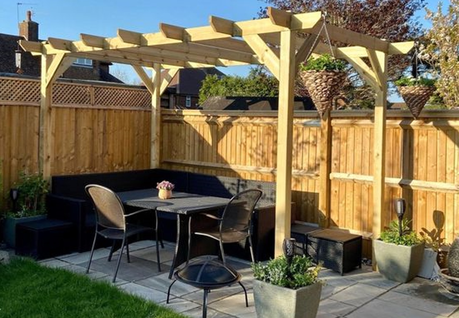 Outdoor patio with pergola, table, chairs, and potted plants in a fenced backyard