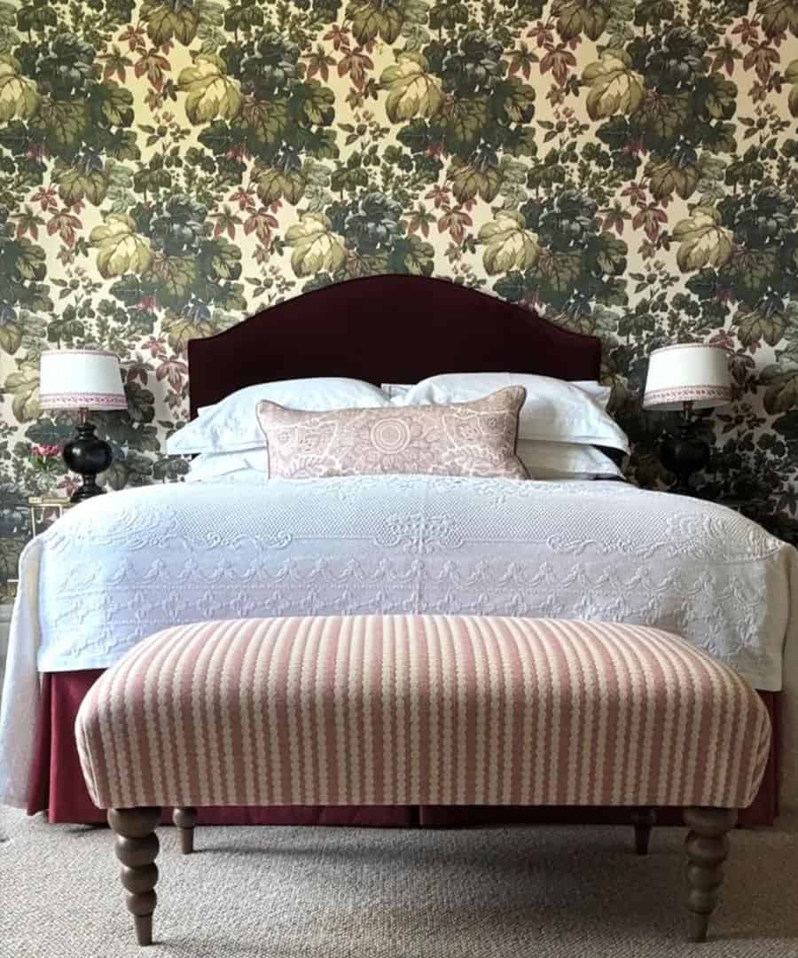 Bedroom featuring floral wallpaper, white linen bed, patterned bench at the foot, and matching lamps on side tables