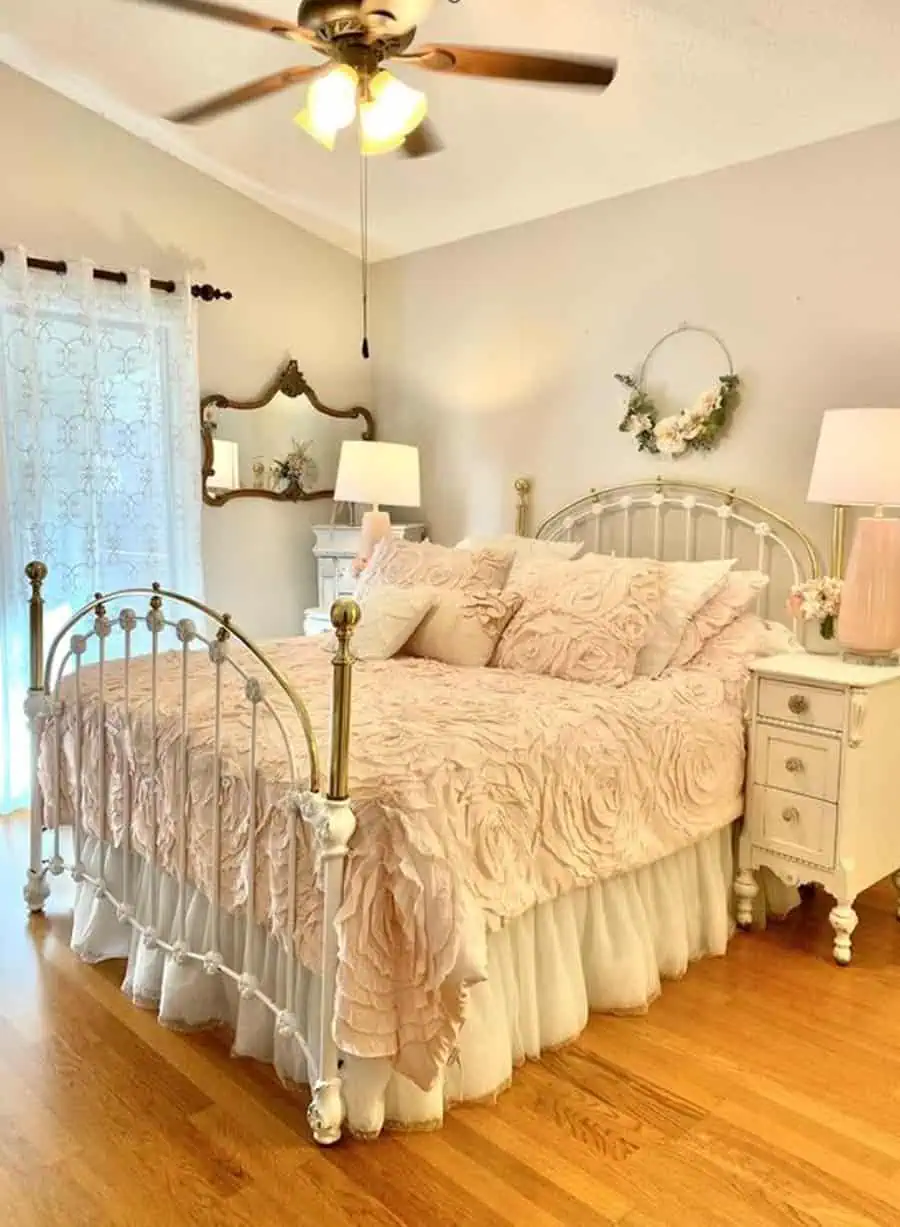 Bedroom featuring a vintage white metal bed with pink bedding, white furniture, floral decor, and a ceiling fan